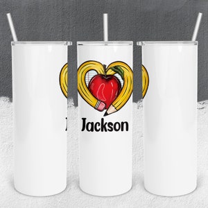 May include: White tumbler with a red apple and two yellow pencils forming a heart shape. The text "Jackson" is printed below the heart.