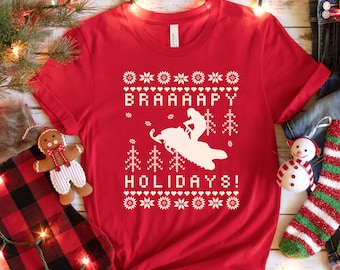 May include: Red t-shirt with a white snowmobile design and the text "BRAAAAPY HOLIDAYS!" in a white, festive font.