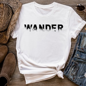 May include: White t-shirt with the word "WANDER" printed in black. The letters are filled with a forest silhouette.