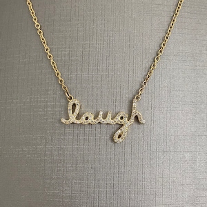 May include: Gold chain necklace with a diamond-encrusted pendant that says "laugh".