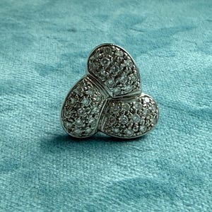 May include: A silver ring with three clover-shaped sections, each covered in small, clear stones.