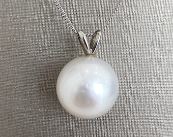 Puede incluir: Un collar con un colgante de perla blanca y una cadena de plata. La perla es grande y redonda, y la cadena es delicada.