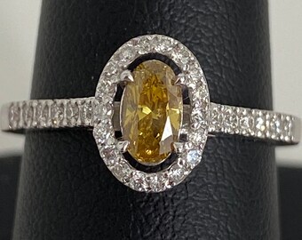 May include: A gold ring with a large oval-shaped yellow diamond surrounded by a halo of smaller diamonds. The ring band is also set with smaller diamonds.