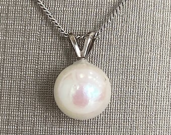 Puede incluir: Un collar con un colgante de perla blanca y una cadena de plata.