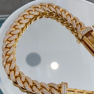 A gold chain bracelet with a clasp. The chain is made of small, interlocking links that are covered in small, clear diamonds.
