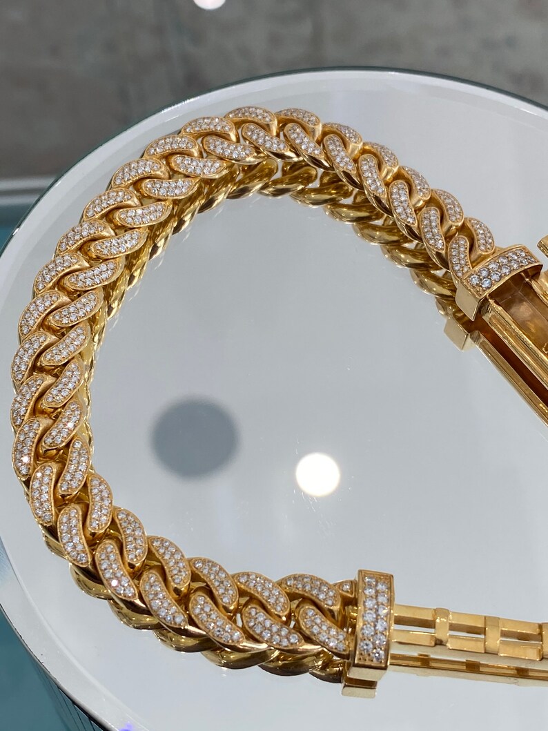 A gold chain bracelet with a clasp. The chain is made of small, interlocking links that are covered in small, clear diamonds.