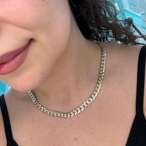 May include: A gold-toned chain necklace with a curb link design. The necklace is worn around the neck and has a shiny, polished appearance. The chain is made of metal and has a classic, timeless style. The necklace is a piece of jewelry.