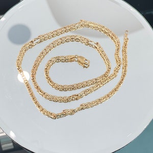 May include: A gold chain necklace with a mariner link design. The chain is laid out on a white surface.