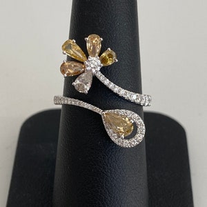 May include: A white gold ring featuring a pear-shaped yellow diamond and a cluster of smaller yellow diamonds set in a flower design.