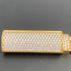 A gold bracelet sliding lock with a diamond-encrusted design. The lighter is rectangular and has a smooth, polished surface.