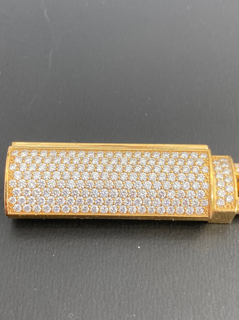 A gold bracelet sliding lock with a diamond-encrusted design. The lighter is rectangular and has a smooth, polished surface.
