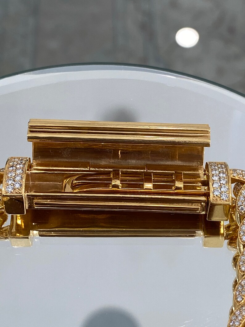 A gold chain bracelet with a diamond-encrusted clasp. The clasp is open, revealing a gold interior with a series of small, rectangular compartments.