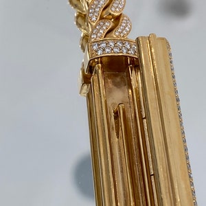 A gold chain bracelet with a clasp. The bracelet is covered in small, clear diamonds. The clasp is a hinged design with a series of vertical lines.