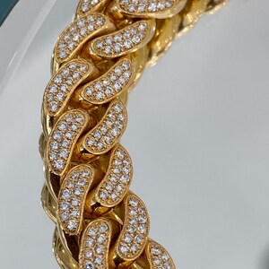 A gold chain with a curb link design. The chain is covered in small, clear, round stones.