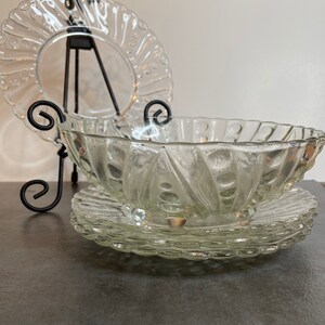 May include: A set of clear glass serving dishes with a decorative, swirling pattern. The dishes are stacked on top of each other, with a large bowl on top and two smaller plates underneath.
