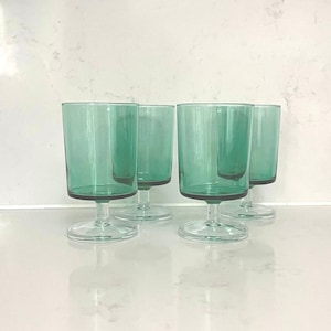 May include: Set of four green glass wine glasses with a clear stem and base.