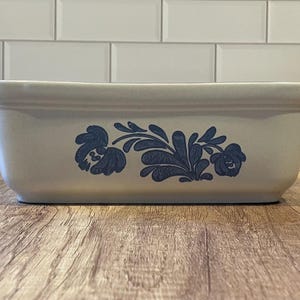 May include: Rectangular, off-white ceramic baking dish with blue floral design. The dish has two small handles and is approximately 12 inches long. Ideal for baking casseroles and other dishes.