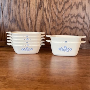 May include: A set of six white ceramic baking dishes with blue floral designs. The dishes are stacked in two groups of three.