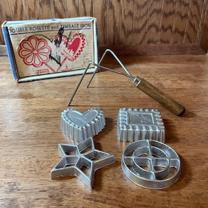 May include: Vintage double rosette and timbale iron set with four decorative cookie molds: heart, square, star, and circle. The set includes a handle and a box with the product name.
