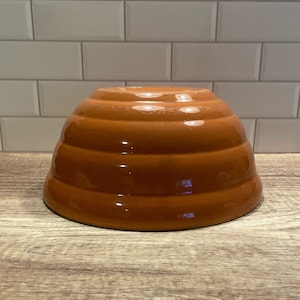 May include: A brown ceramic honey pot shaped like a beehive with five ridges.