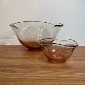 May include: Two glass bowls with a wavy rim. The larger bowl is clear with a pink tint at the bottom. The smaller bowl is a solid pink color.