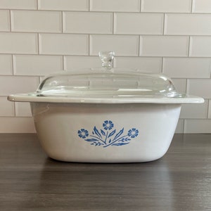 May include: White ceramic casserole dish with a blue floral design and a clear glass lid.