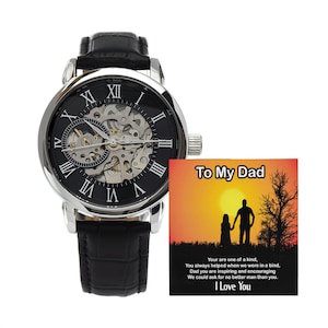 May include: A silver and black skeleton watch with Roman numeral markings on the face, a black leather band, and a small card with the text "To My Dad" and a message about appreciation.