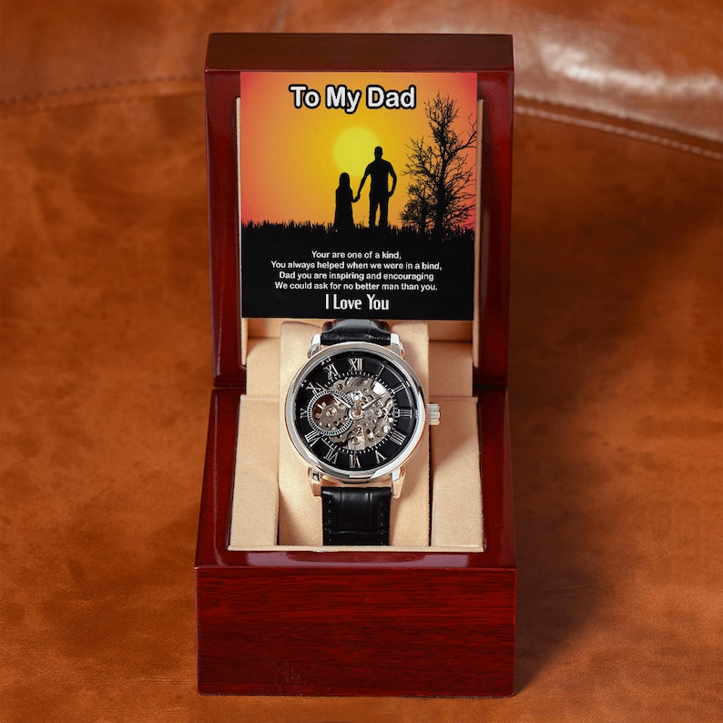 May include: A silver and black watch with a skeleton movement in a red wooden box. The box has a card inside with the text "To My Dad" and a message about how great dads are.