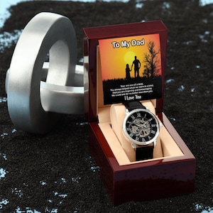 May include: A silver watch with a black leather band in a wooden box. The box has a message that reads "To My Dad" and a silhouette of a father and daughter walking in a sunset. The message reads "You are one of a kind, You always helped when we were in a bind, Dad you are inspiring and encouraging We could ask for no better man than you. I Love You."