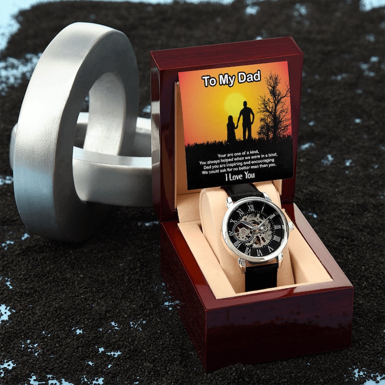 May include: A silver watch with a black leather band in a wooden box. The box has a message that reads "To My Dad" and a silhouette of a father and daughter walking in a sunset. The message reads "You are one of a kind, You always helped when we were in a bind, Dad you are inspiring and encouraging We could ask for no better man than you. I Love You."