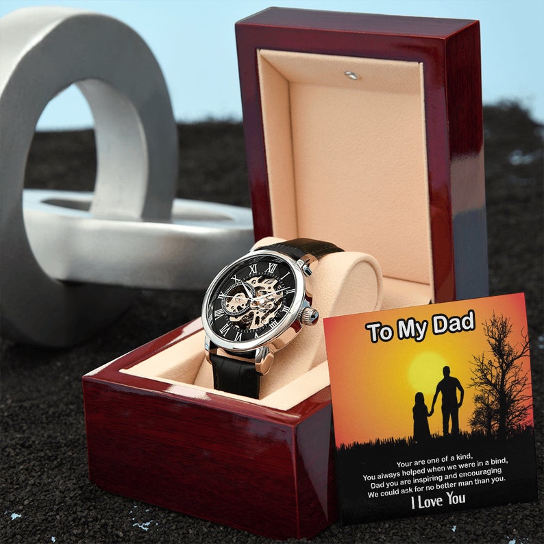 May include: A black and silver watch with a skeleton dial in a red wooden box. The box also includes a card with the text "To My Dad" and a message about how great dads are.