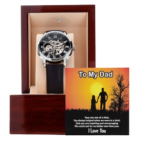 May include: A silver and black automatic watch with a black leather band in a wooden box. The box includes a card with the text "To My Dad" and a silhouette of a father and child walking hand-in-hand in front of a sunset. The card reads "Your are one of a kind, You always helped when we were in a bind, Dad you are inspiring and encouraging We could ask for no better man than you. I Love You."