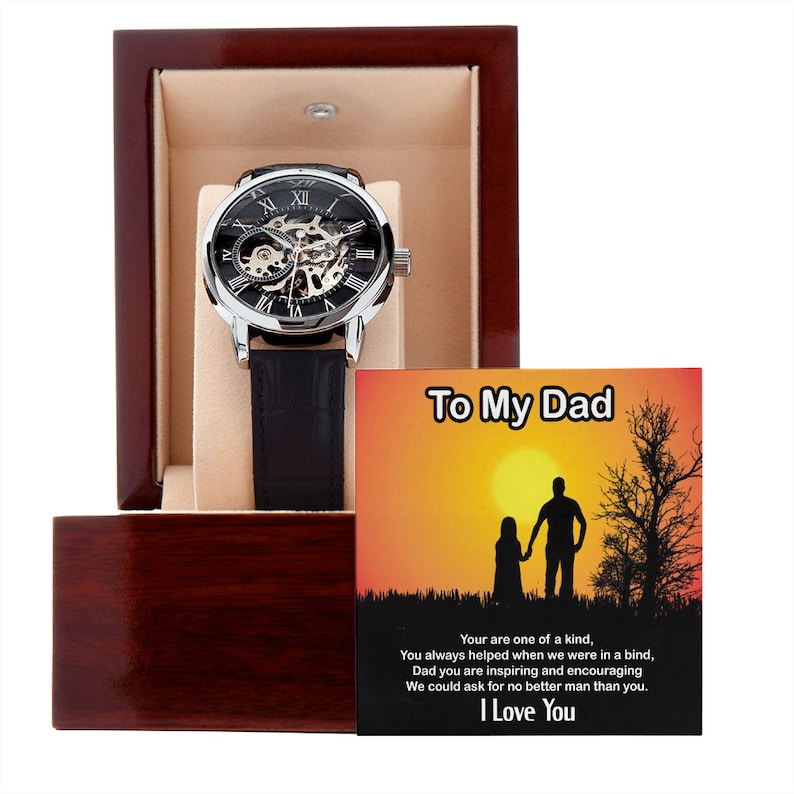May include: A silver and black automatic watch with a black leather band in a wooden box. The box includes a card with the text "To My Dad" and a silhouette of a father and child walking hand-in-hand in front of a sunset. The card reads "Your are one of a kind, You always helped when we were in a bind, Dad you are inspiring and encouraging We could ask for no better man than you. I Love You."