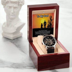 May include: A wooden box with a watch inside. The box is red with a gold interior. The watch has a black face with Roman numerals and a silver band. The box has a message inside that reads "To My Dad".