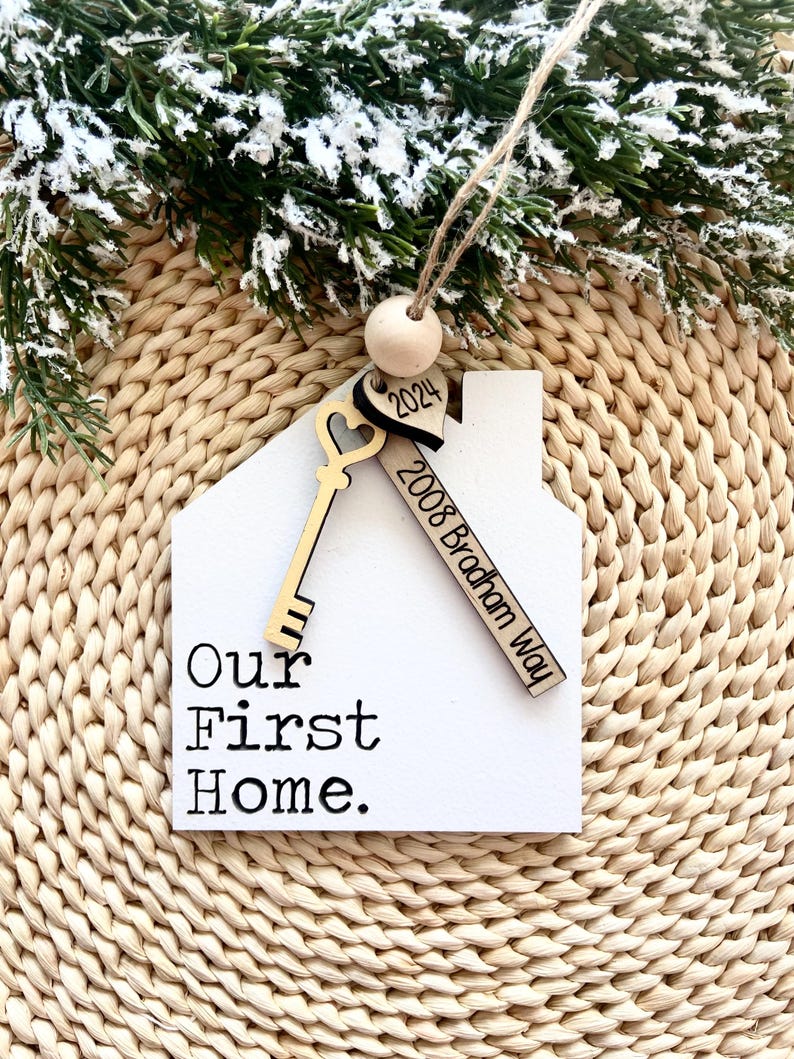 May include: White wooden house-shaped ornament with a key and heart charm. The ornament says "Our First Home" and "2008 Bradham Way" and "2024".
