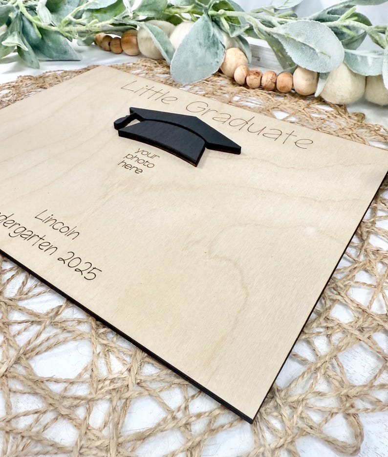 May include: A wooden graduation photo frame with the words "Little Graduate" and "your photo here" engraved. A black mortarboard is affixed to the frame. The name "Lincoln" and the year "2025" are also engraved.