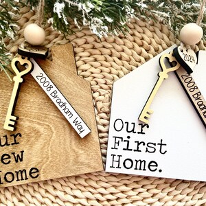 May include: Two wooden house-shaped ornaments with gold keys and a white tag that says "2008 Bradham Way". One ornament is brown and says "Our New Home". The other ornament is white and says "Our First Home."
