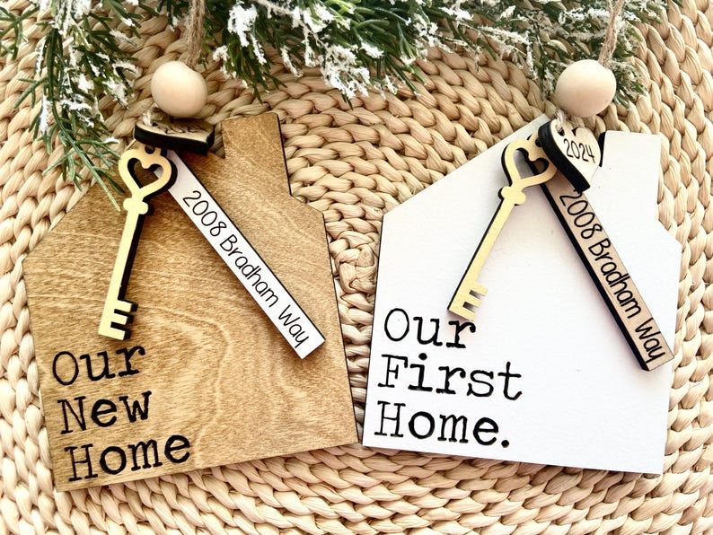 May include: Two wooden house-shaped ornaments with gold keys and a white tag that says "2008 Bradham Way". One ornament is brown and says "Our New Home". The other ornament is white and says "Our First Home."