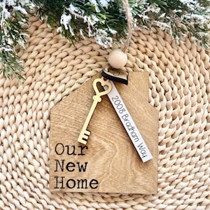 May include: Wooden house-shaped ornament with a gold key and a tag that reads "2008 Bradham Way". The ornament also has the text "Our New Home" engraved on it.