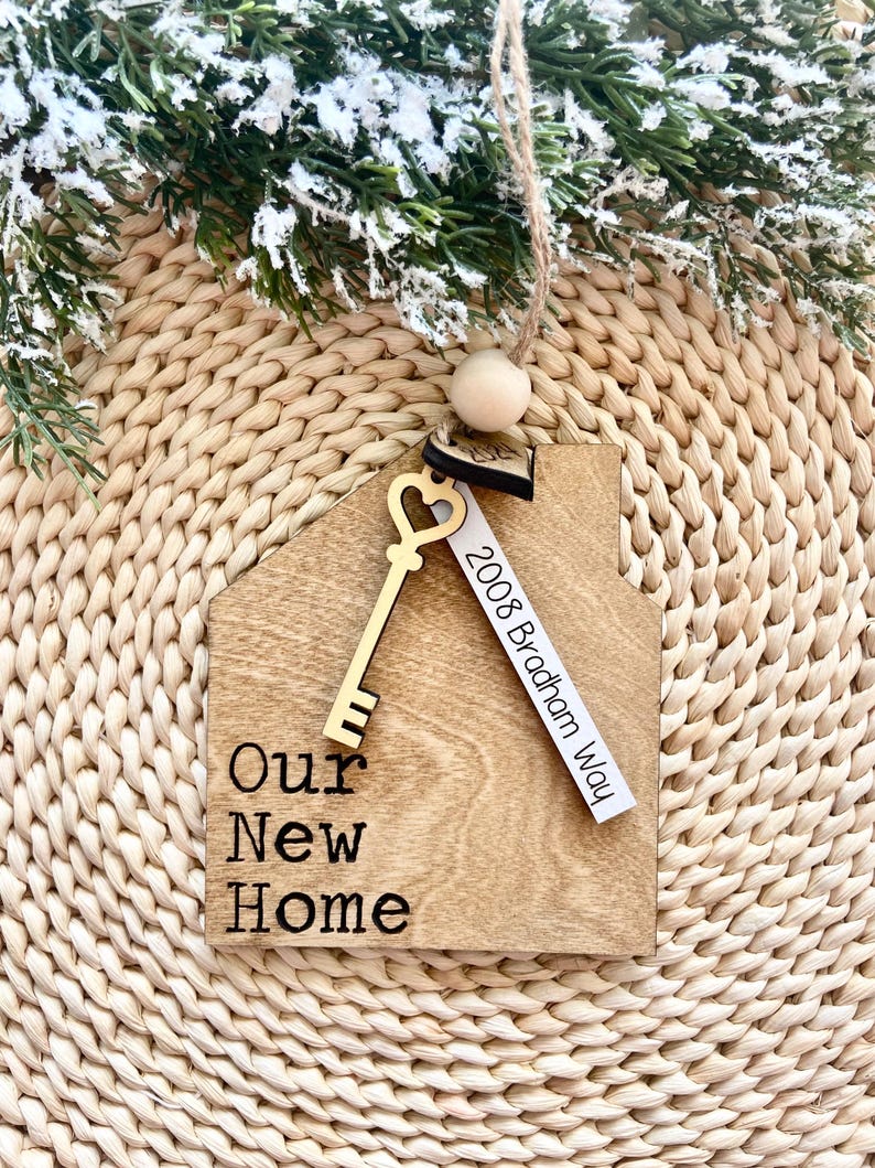 May include: Wooden house-shaped ornament with a gold key and a tag that reads "2008 Bradham Way". The ornament also has the text "Our New Home" engraved on it.