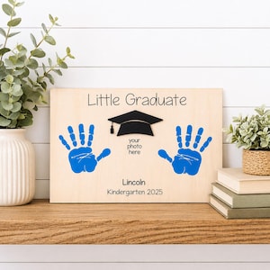 May include: Wooden graduation keepsake with blue handprints, a black graduation cap, and the text "Little Graduate." Includes space for a photo and the name "Lincoln" with the year "Kindergarten 2025."