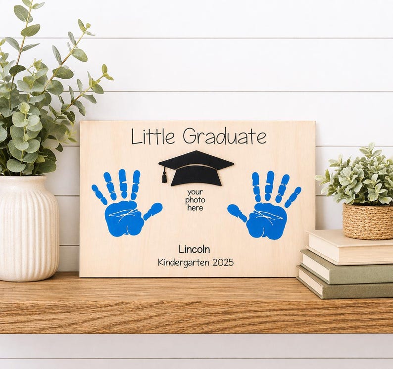 May include: Wooden graduation keepsake with blue handprints, a black graduation cap, and the text "Little Graduate." Includes space for a photo and the name "Lincoln" with the year "Kindergarten 2025."