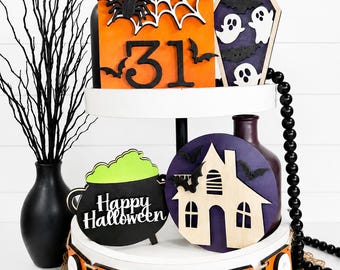 May include: A two-tiered white tray featuring Halloween-themed wooden decorations including a sign with the number 31, a coffin with ghosts, a cauldron with green liquid labeled Happy Halloween, a haunted house, and a banner spelling BOO.