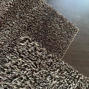 May include: Close-up of a textured, brown and white rug. The rug has a shaggy appearance with a dense pile of fibers. The fibers are a mix of brown and white, creating a speckled effect. The rug is on a dark brown surface.