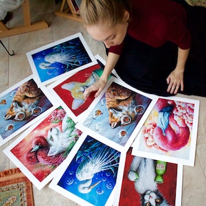 Puede incluir: Una colecci&oacute;n de 10 impresiones de arte con diversas ilustraciones de animales. Las impresiones se muestran en una mesa con una mano apuntando a una de las impresiones. Las impresiones presentan una variedad de animales, incluyendo un flamenco, un gato, un zorro, un p&aacute;jaro y un gato.