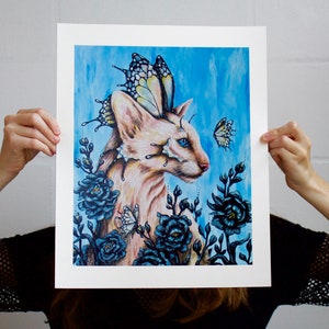 Puede incluir: Un gato blanco con alas de mariposa y ojos azules est&aacute; rodeado de flores azul oscuro. El gato mira hacia la derecha. El fondo es una acuarela azul claro.