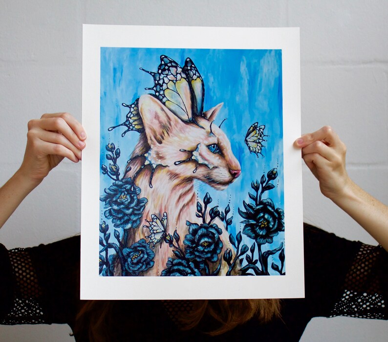 Puede incluir: Un gato blanco con alas de mariposa y ojos azules est&aacute; rodeado de flores azul oscuro. El gato mira hacia la derecha. El fondo es una acuarela azul claro.