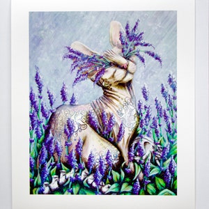 K&ouml;nnte beinhalten: Eine wei&szlig;e haarlose Katze mit einem floralen Tattoo sitzt in einem Feld mit lila Lavendelbl&uuml;ten. Die Augen der Katze sind geschlossen und die Blumen bedecken ihren Kopf.