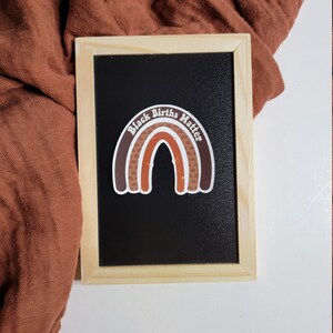 May include: A black chalkboard with a brown and white rainbow sticker that says "Black Births Matter".
