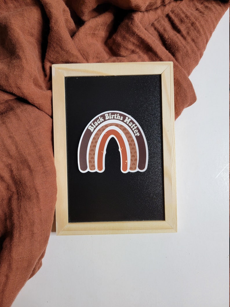May include: A black chalkboard with a brown and white rainbow sticker that says "Black Births Matter".